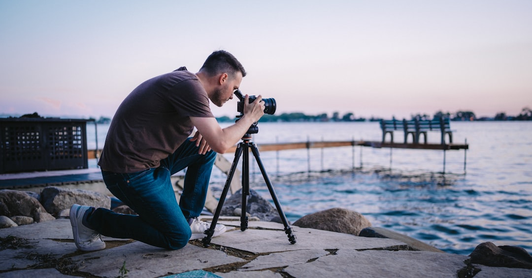 Photographer kneeling beside water setting up a camera on a tripod for a landscape shot