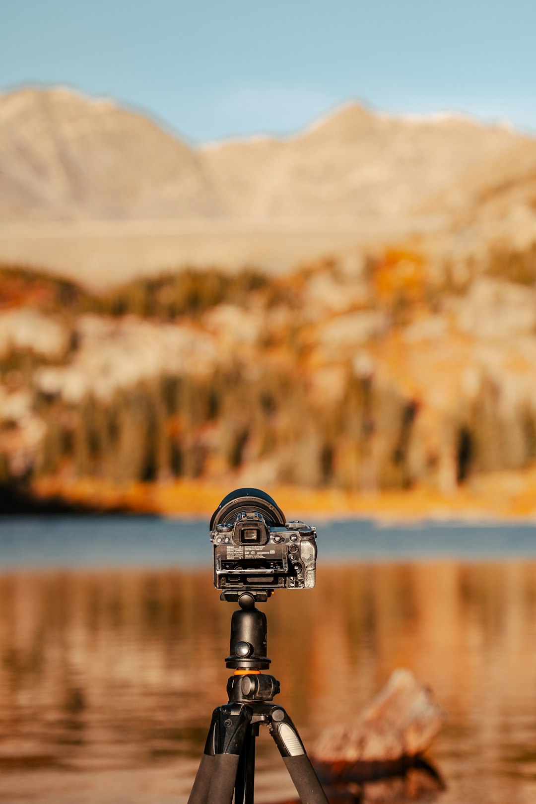 Camera on a tripod set up for landscape photography beside a mountain lake